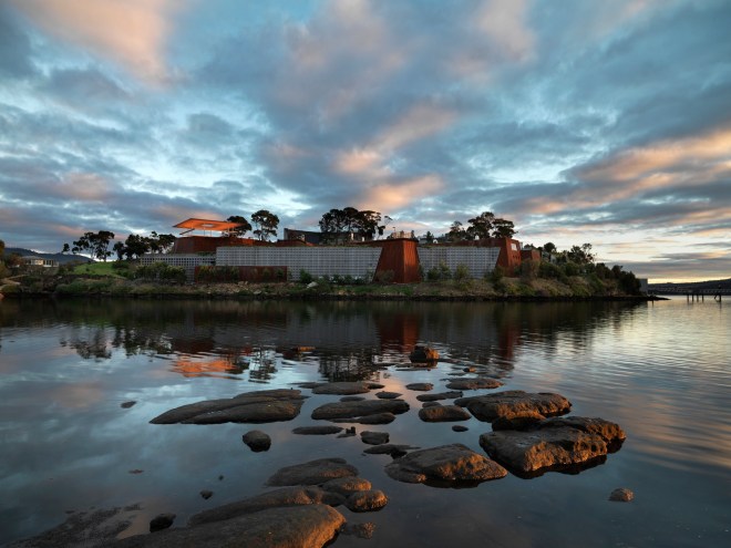 MONA, Museum of Old and New Art Mona's southern facade viewed from Little Frying Pan Island, south of the museum, and view of Amarna (2015) Skyspace installation during dawn sequence. AMARNA 2015 James Turrell (born 1943, Los Angeles, California; lives and works in Flagstaff, Arizona) Skyspace series Dimensions: 7 (H) 28.3 x (W) x 21.15m (D) Museum rooftop plaza Steel frame, fibreglass foam sandwich roof construction, fibreglass reinforced concrete seating Copyright James Turrell Photo credit: MONA/Rémi Chauvin Image courtesy of MONA Museum of Old and New Art, Hobart, Tasmania, Australia